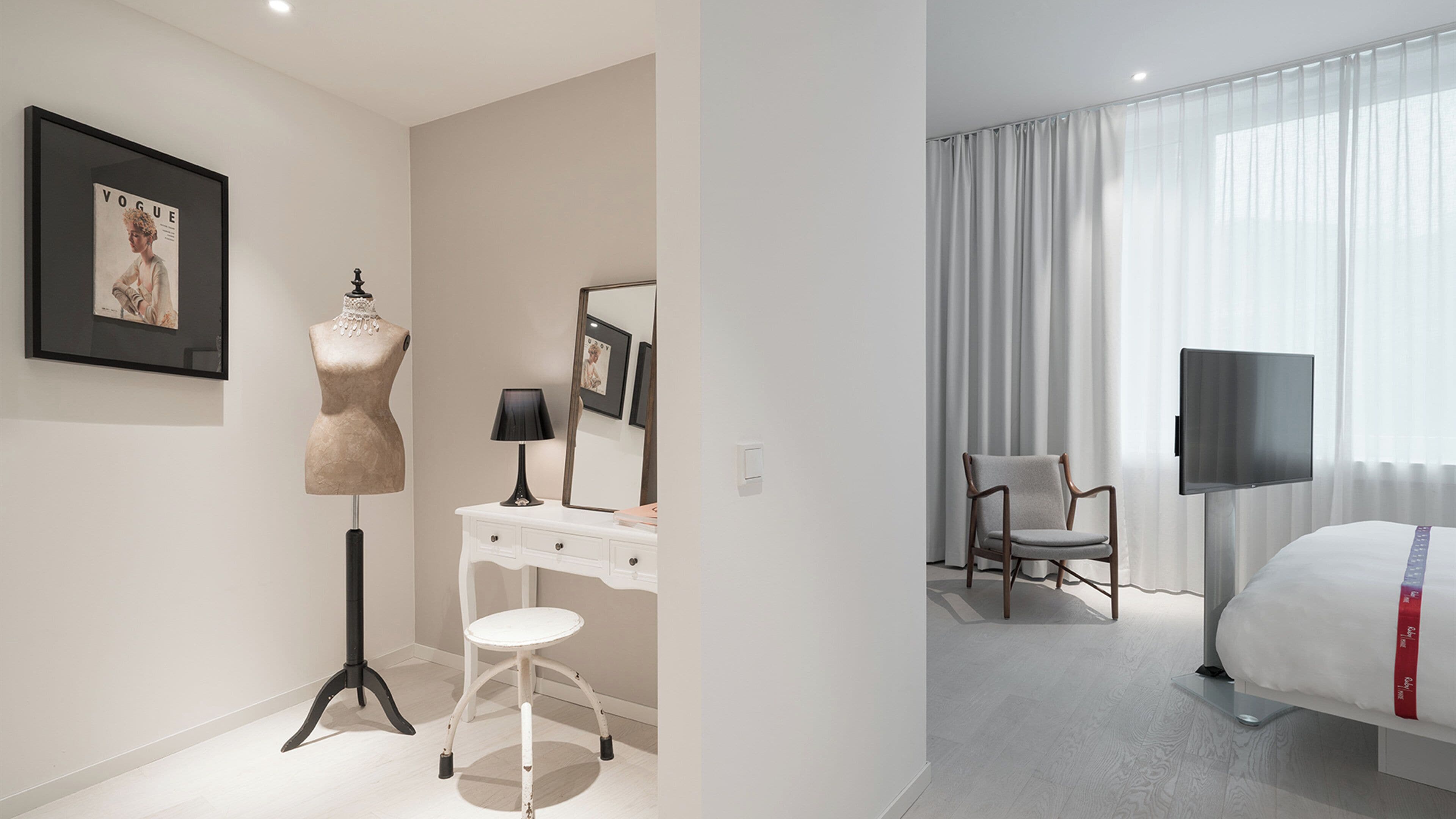 A modern hotel room with a bed, a desk, a chair, a lamp, and a large window with curtains.