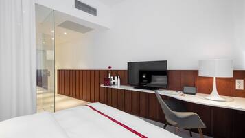 A modern hotel room with a bed, a desk with a computer, a television, and a lamp.