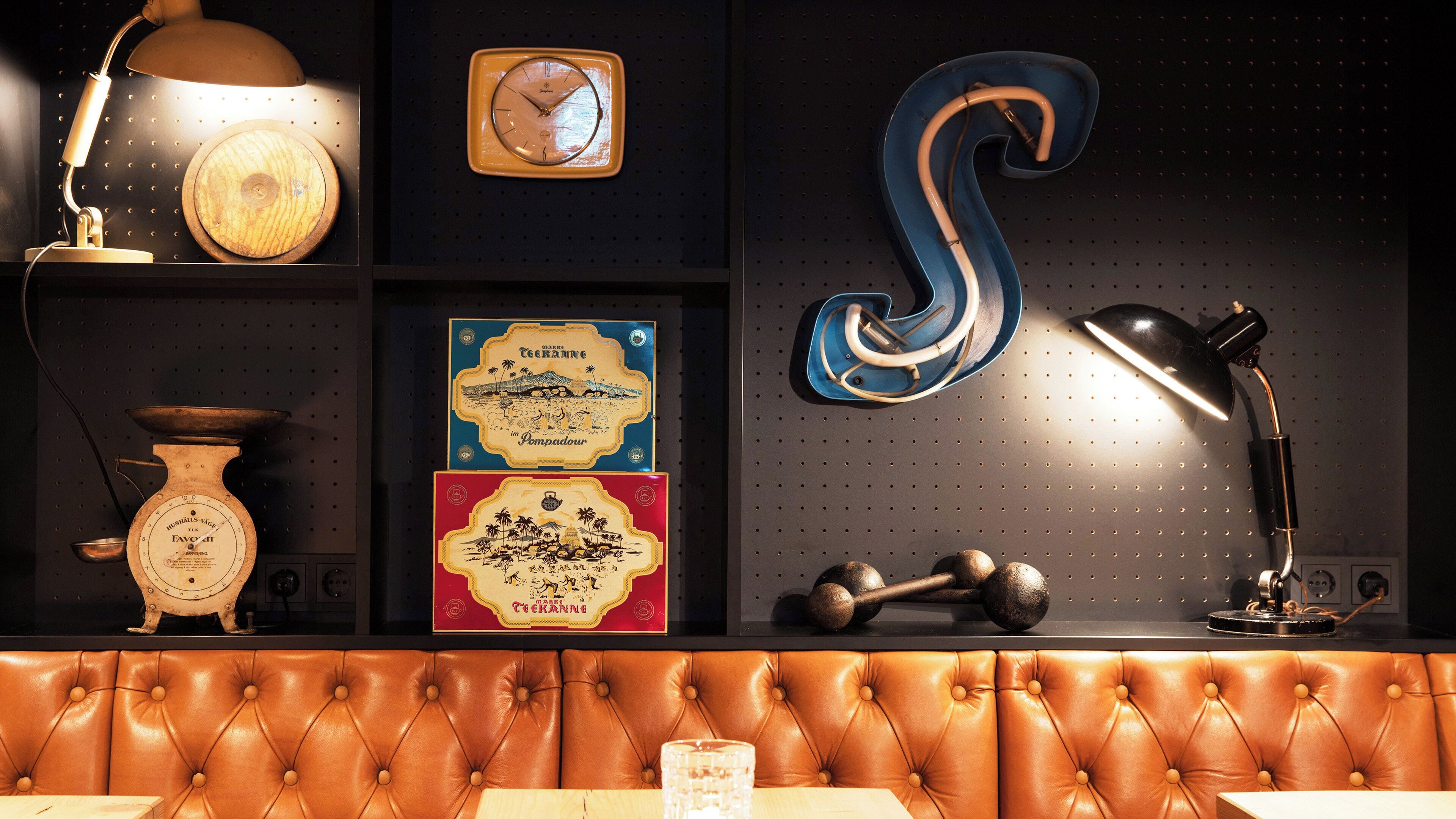 A room with a tufted leather bench, a wall clock, a decorative wall piece, a scale, and a framed picture.