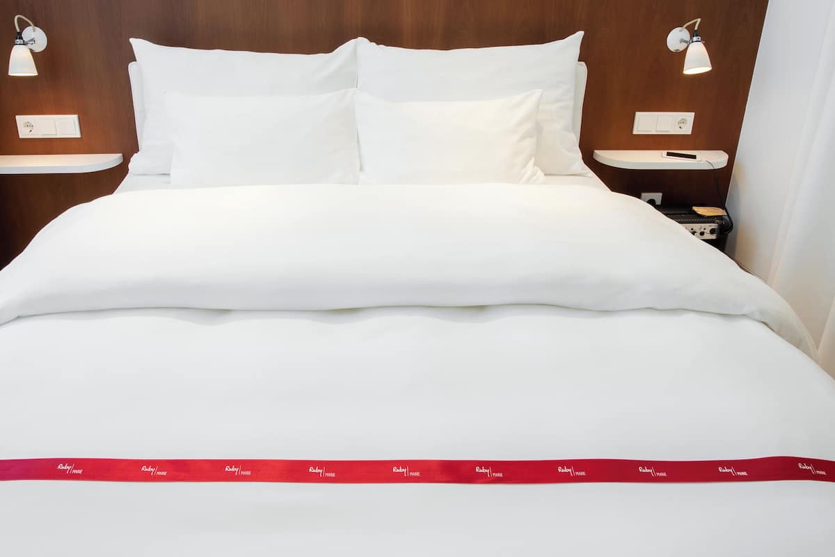 A neatly made bed with white bedding, two bedside tables with lamps, and a red ribbon on the bedspread.