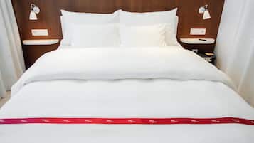 Una cama bien hecha con ropa blanca, dos mesitas de noche con lámparas y un lazo rojo sobre la colcha.