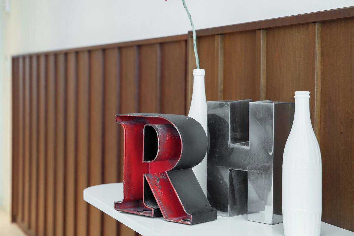 A reception desk with a wooden panel backdrop, a white counter, and a red and black letter 'RH' sign.
