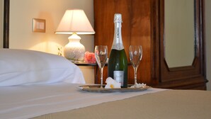 A hotel room with a bed, a nightstand with a lamp, a bottle of champagne, and two glasses. - Villa Quiete (Spadafora)