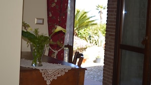 A wooden table with a lace tablecloth, a vase with green plants, and a chair. - Villa Quiete (Spadafora)