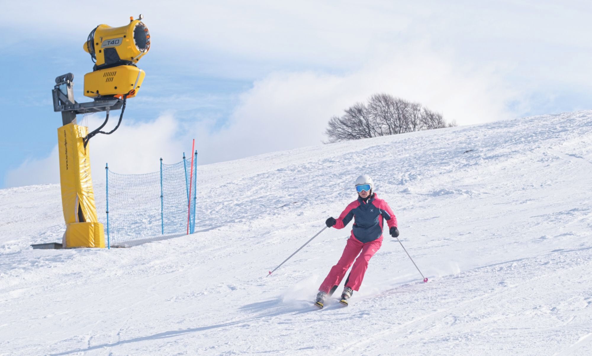 Eine Person fährt auf Skiern einen verschneiten Hang hinunter, links ist ein gelbes Objekt zu sehen.