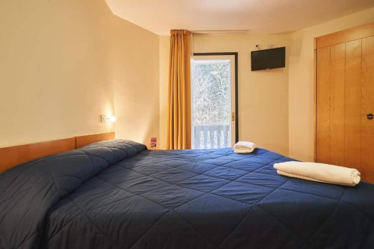 Een hotelkamer met een groot bed, een raam met gordijnen, een televisie aan de muur en een houten deur.