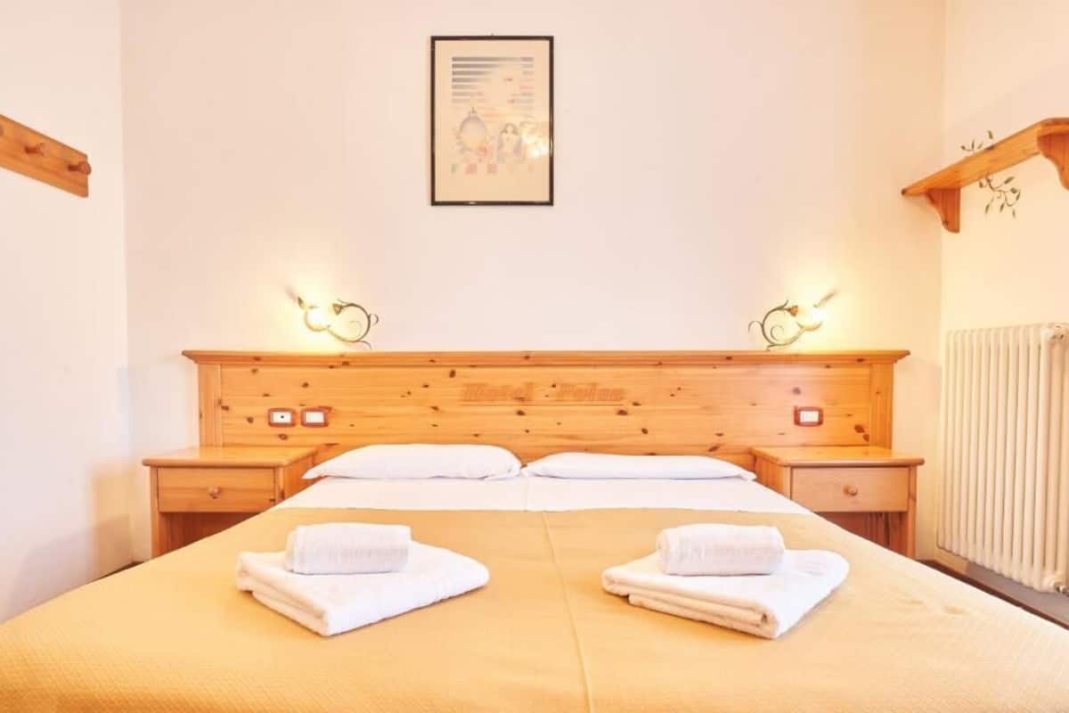 Een hotelkamer met een houten hoofdeinde, twee nachtkastjes, een bed met witte lakens en twee wandlampen.