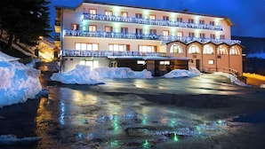 Um hotel com vários andares, varandas, entrada coberta e área de estacionamento com neve.