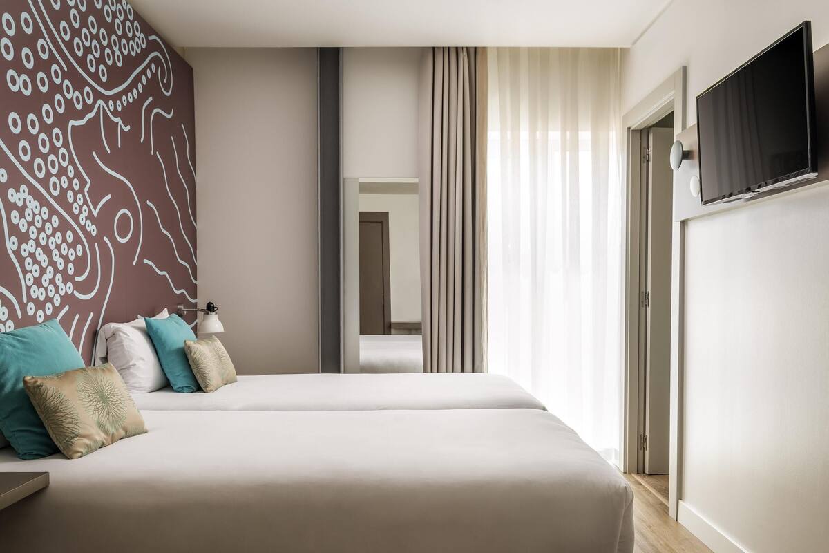 A modern hotel room with a large bed, a flat-screen TV, and a large window with curtains.