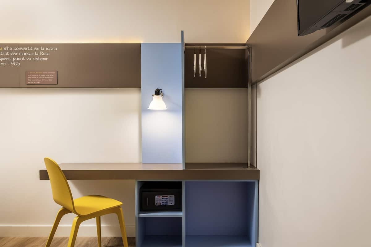 A modern room with a desk, a chair, a shelf with a device, and a wall-mounted light.