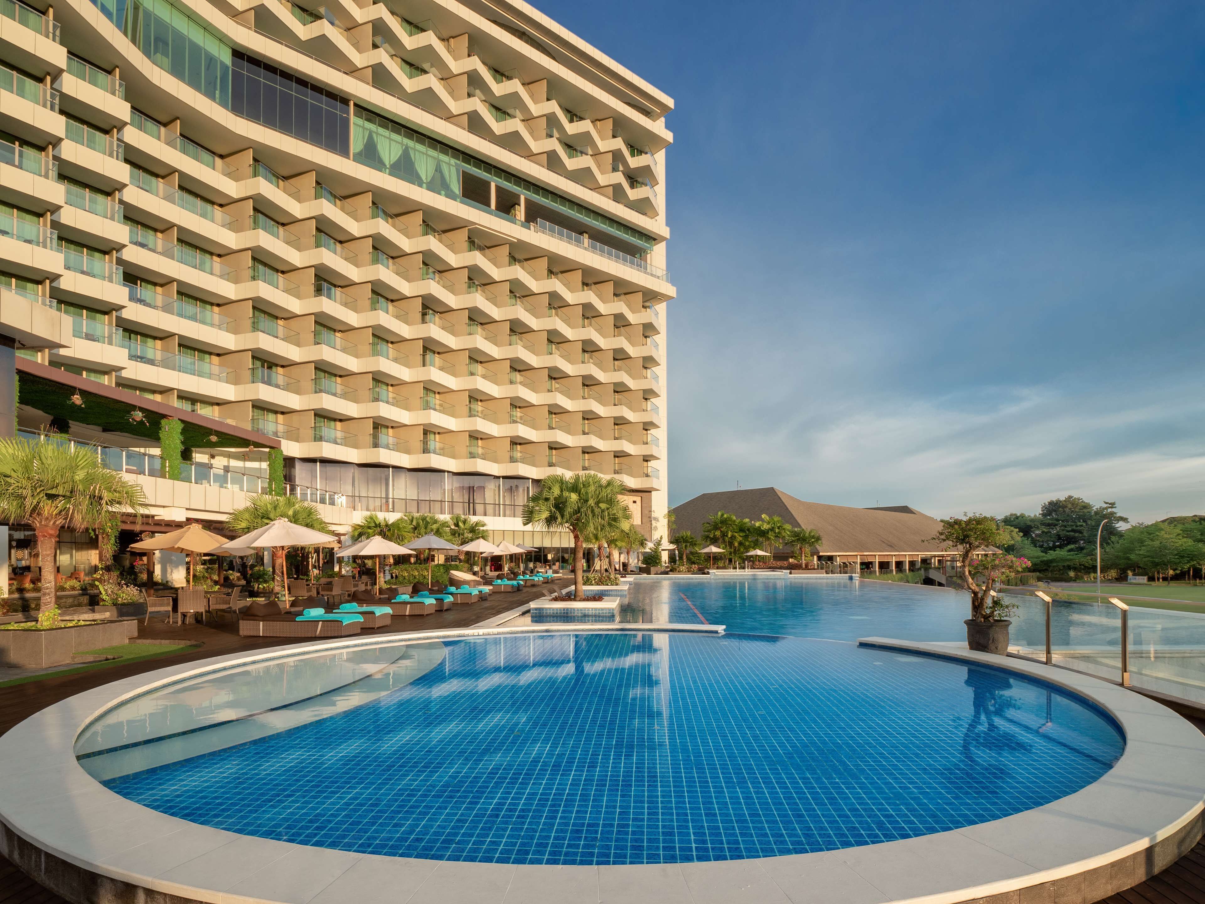 A hotel with a large pool, outdoor seating, and a modern building design.
