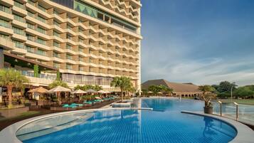 A hotel with a large pool, outdoor seating, and a modern building design.