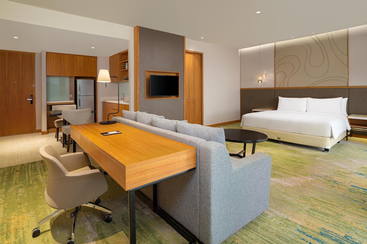 Ein Hotelzimmer mit einem Holztisch, einer grauen Couch und einem weißen Bett.