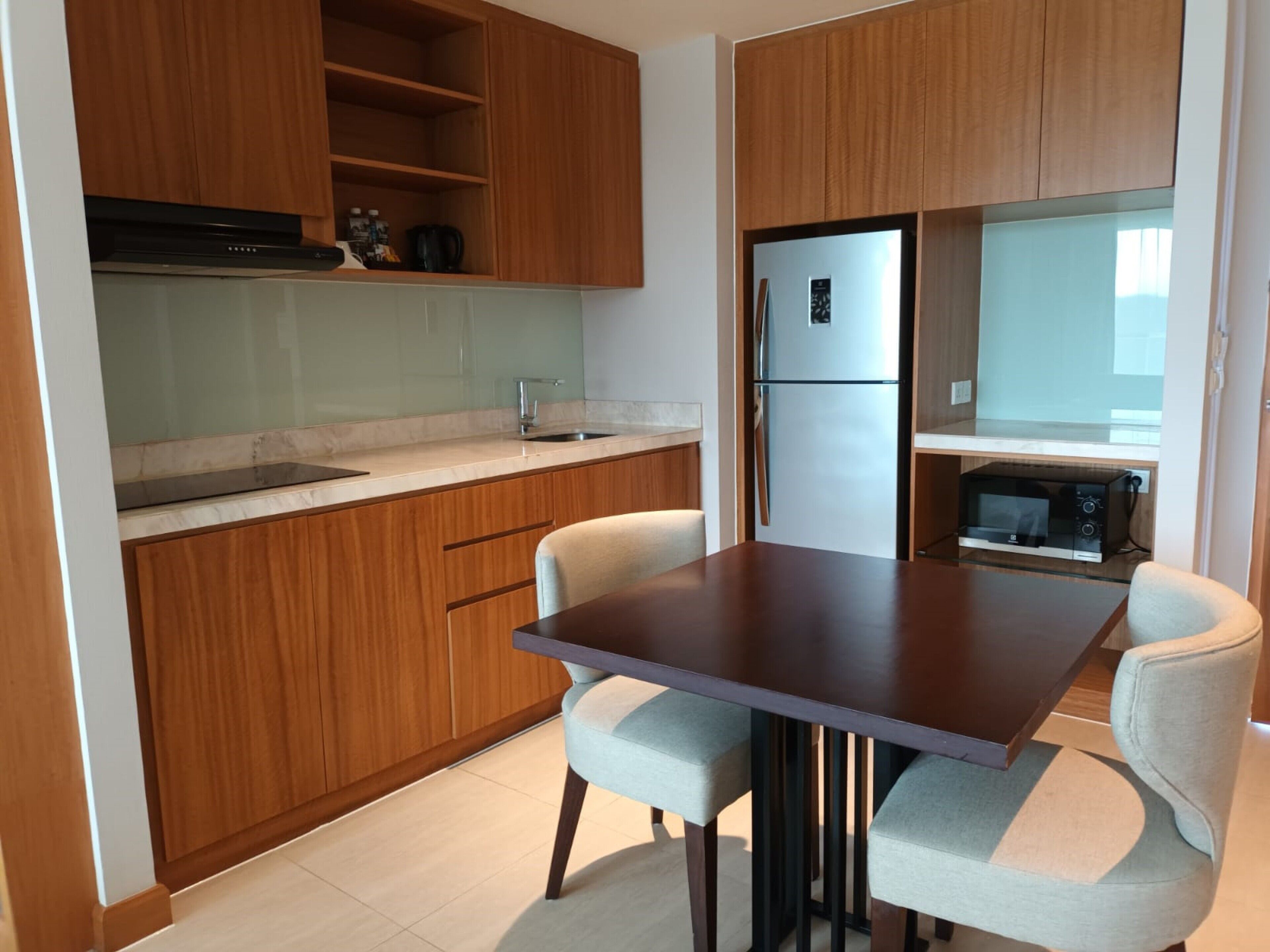Una cocina moderna con armarios de madera, un refrigerador de acero inoxidable, un microondas y una mesa de comedor con dos sillas.