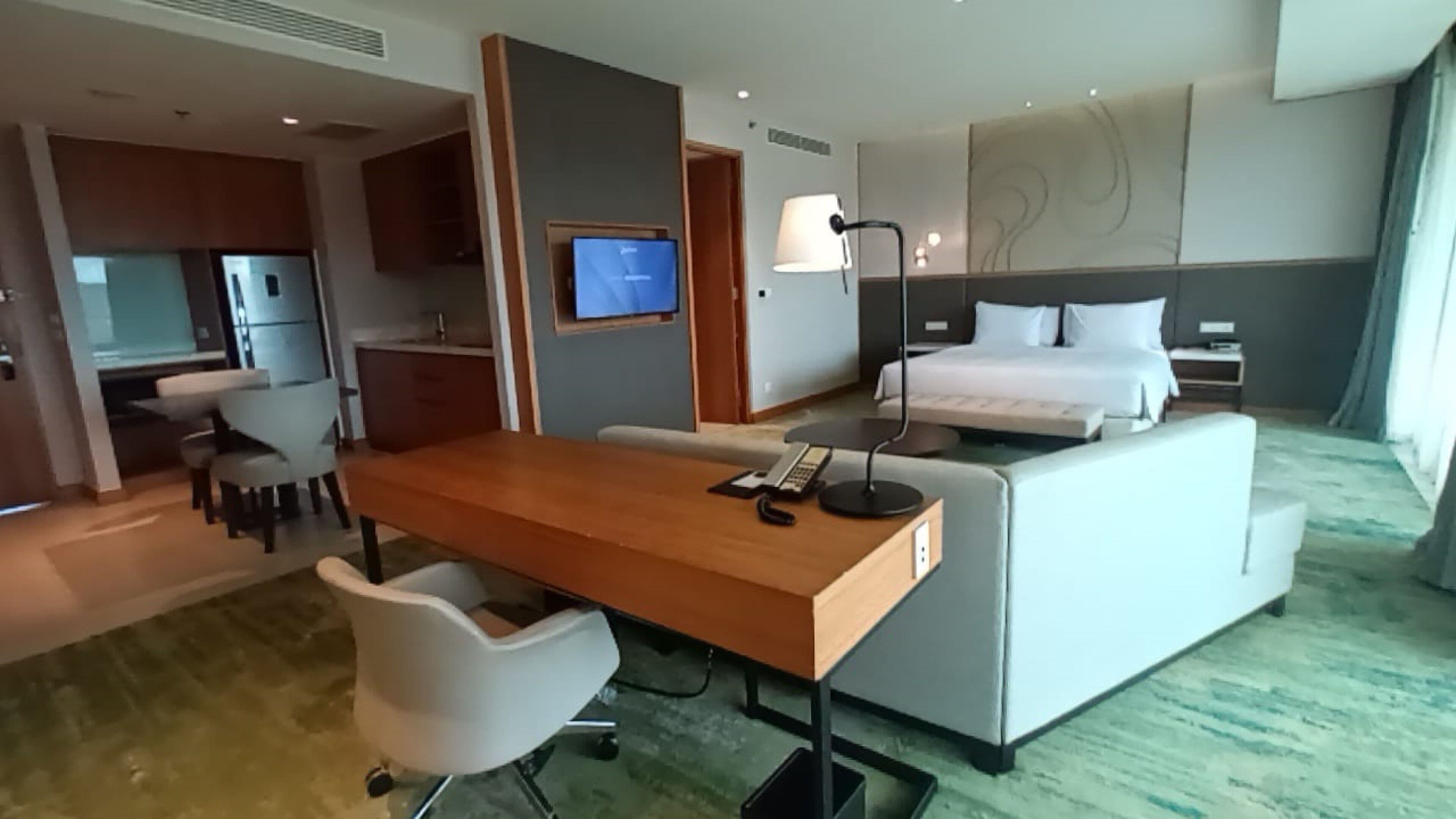 A hotel room with a bed, a desk with a chair, a television, and a lamp.