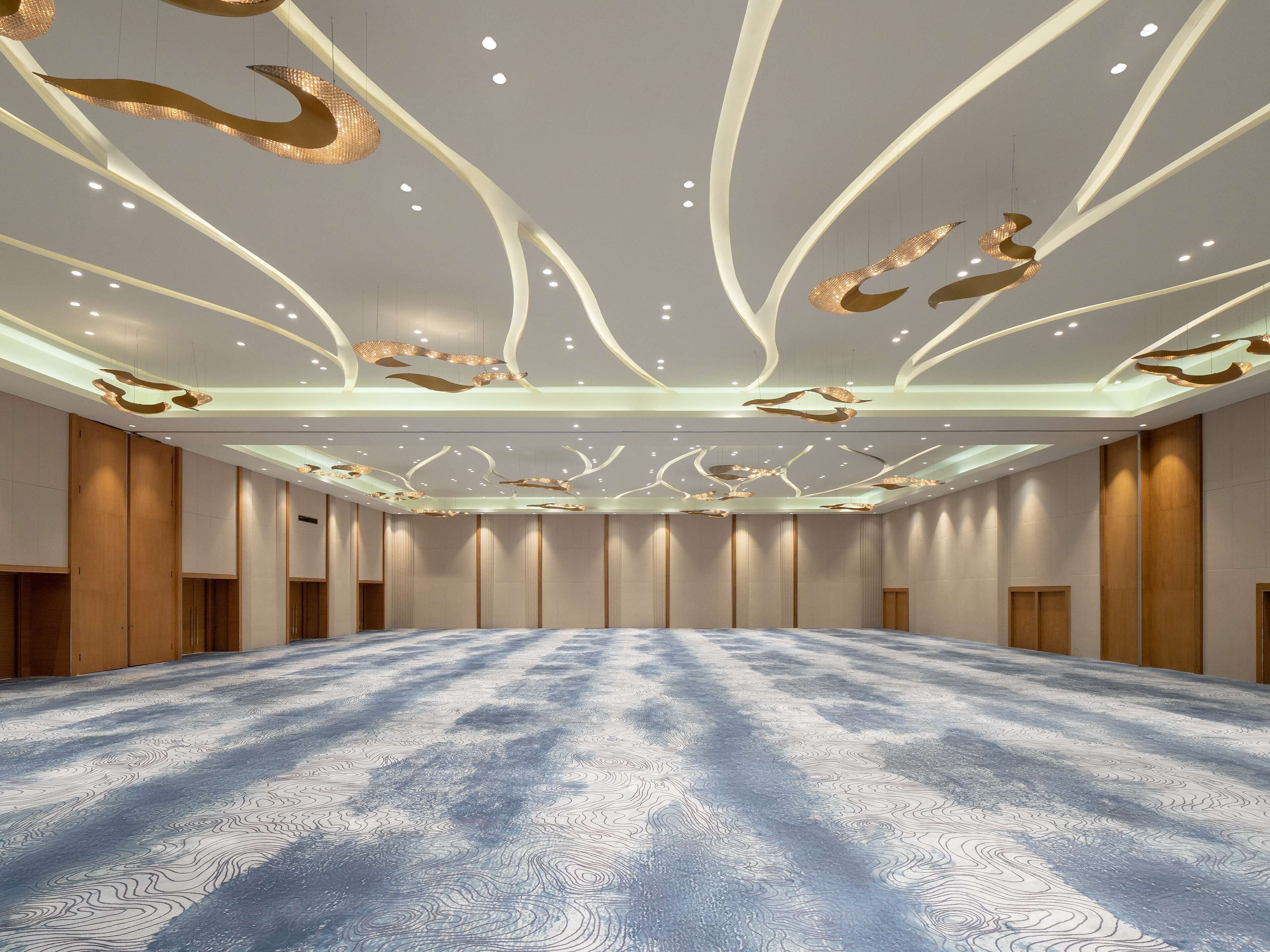 Une salle de conférence spacieuse, dotée d’un tapis à motifs, de murs lambrissés et de luminaires modernes au plafond.