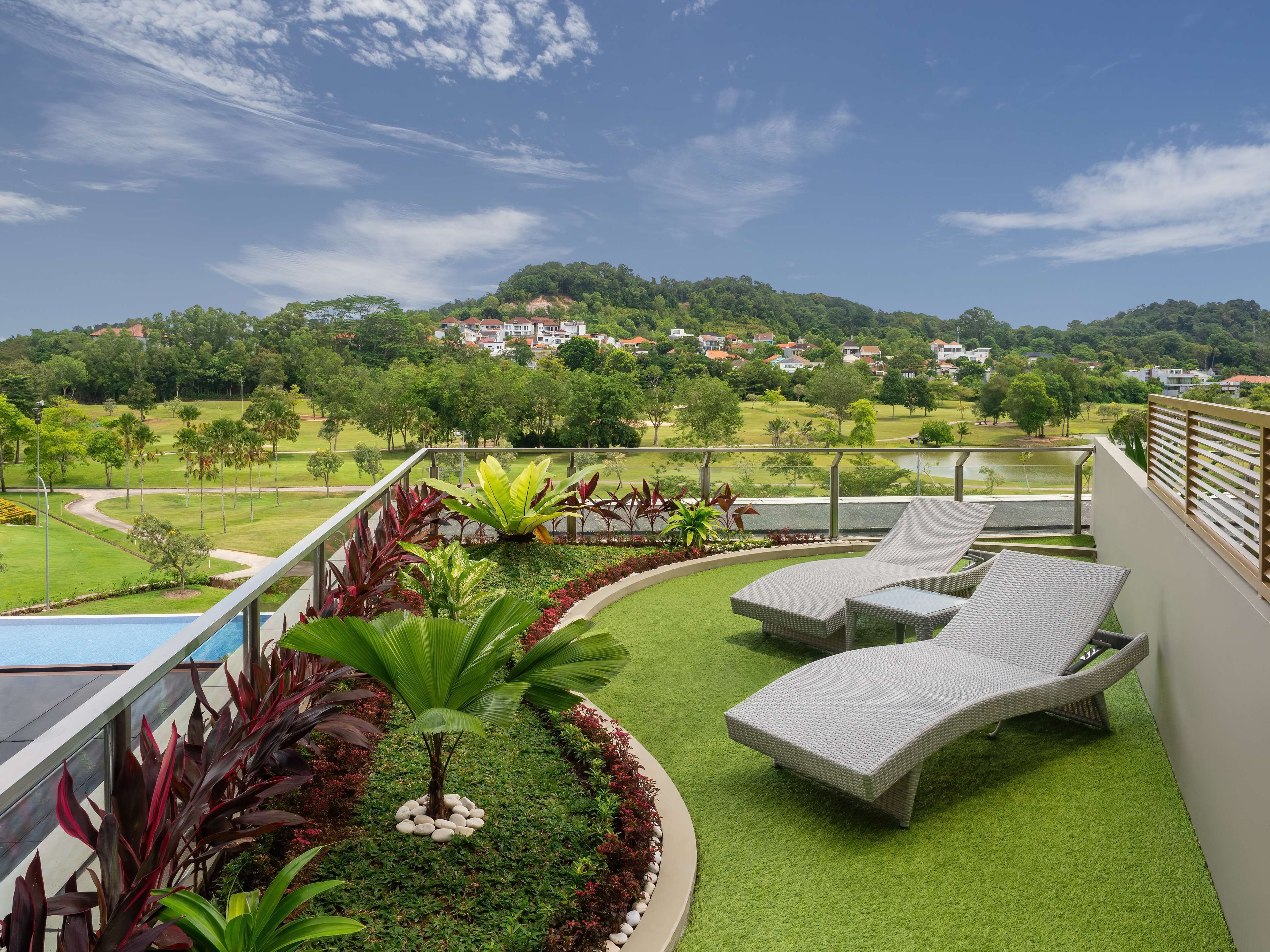 Un balcón con vistas a un campo de golf, una piscina y sillones de descanso.