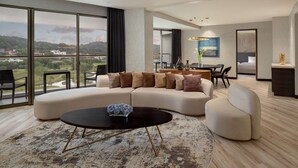 Una sala moderna con un amplio sofá modular, una mesa de centro redonda y vistas a un paisaje verde a través de amplios ventanales.