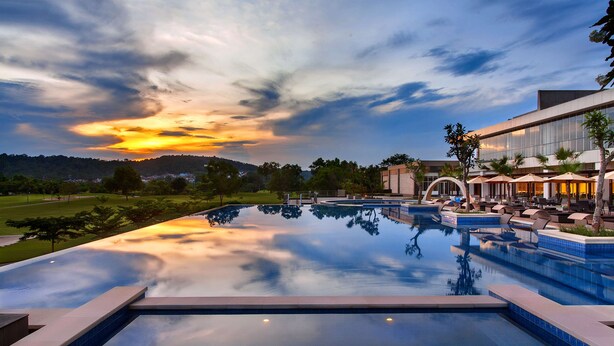 Una amplia piscina infinita con vistas a un atardecer y colinas distantes.