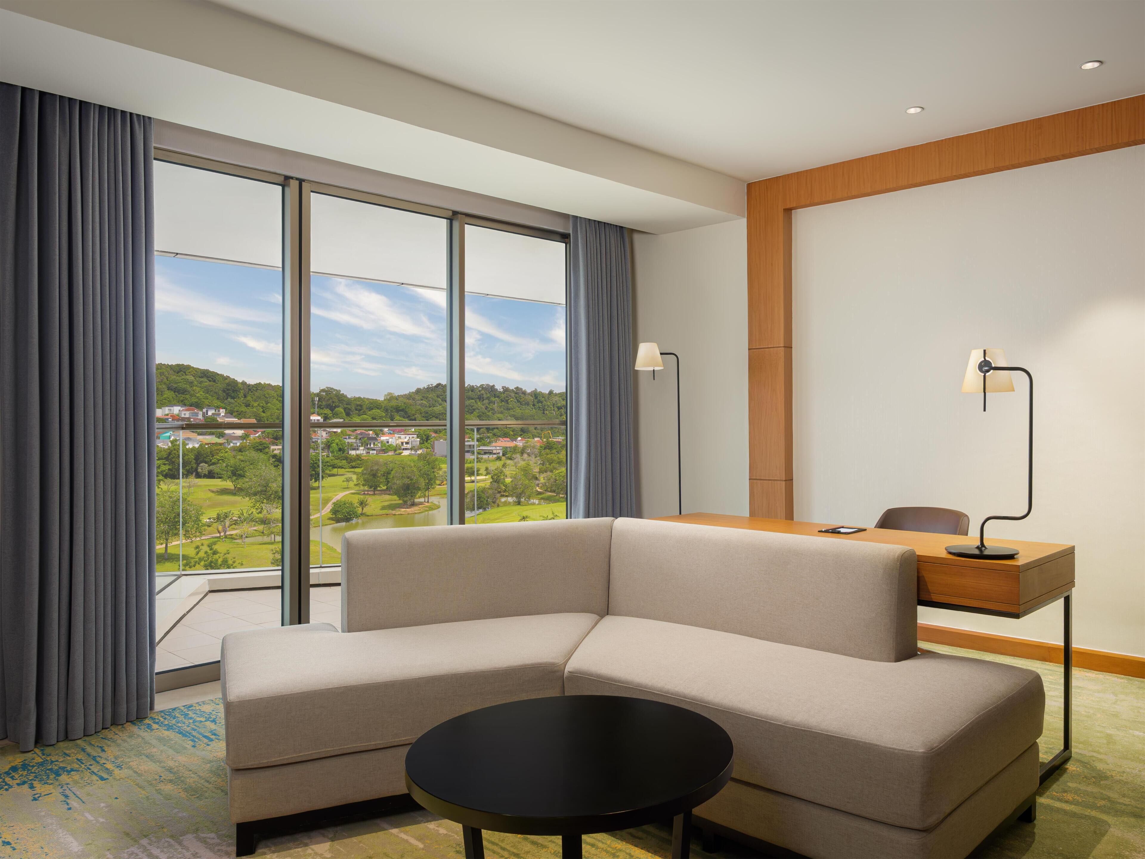 A modern hotel room with a sofa, a small table, a desk, and a lamp.