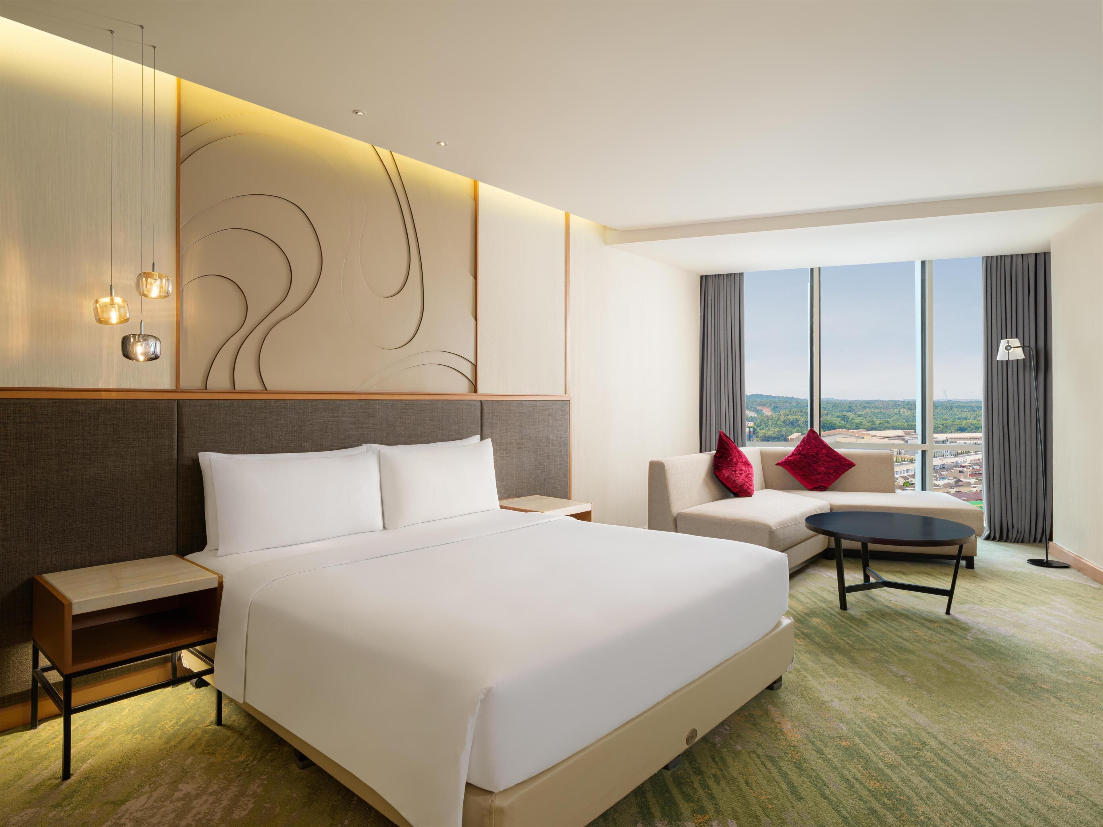 Habitación de hotel con una cama grande, un sofá, una mesita y vistas a la ciudad.