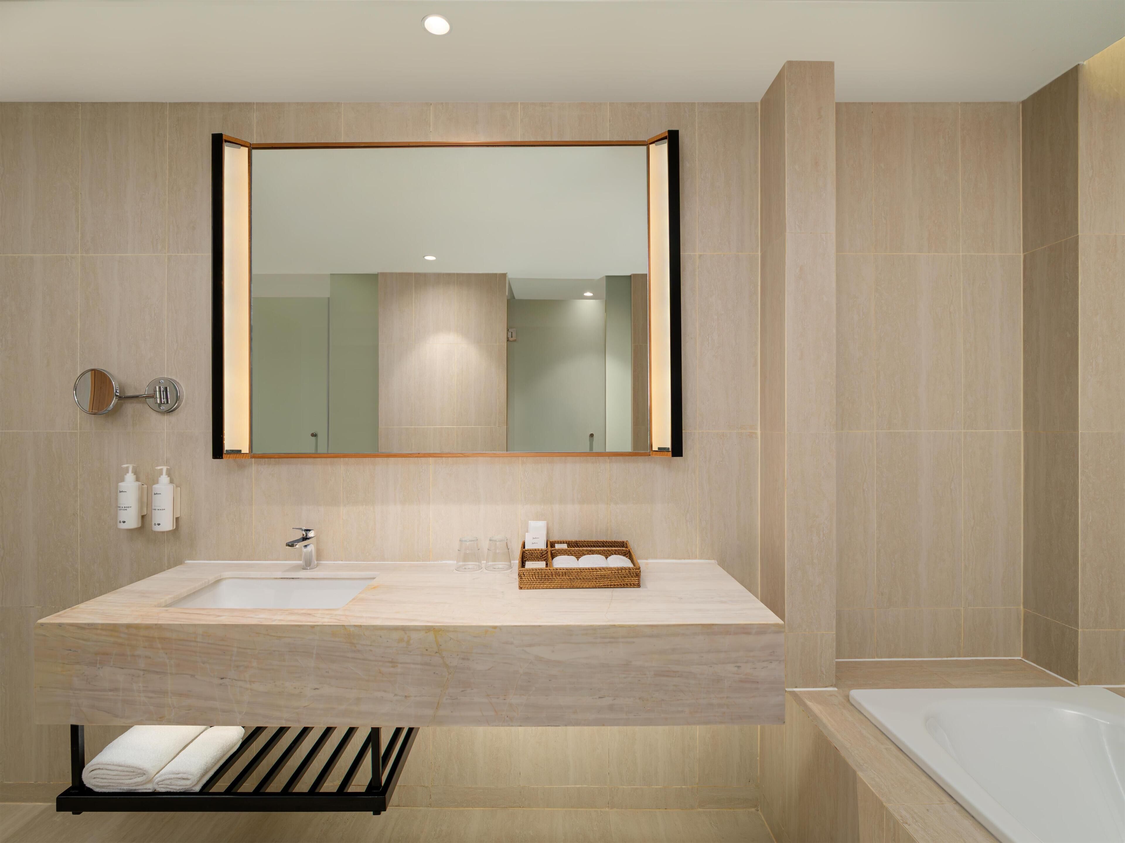 A modern bathroom with a large mirror, two sinks, a bathtub, and a towel rack.