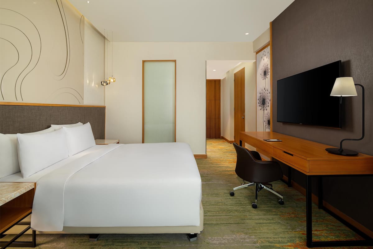 Ein Hotelzimmer mit einem großen Bett, einem Schreibtisch mit Stuhl, einem Fernseher und einer Tür zu einem weiteren Raum.