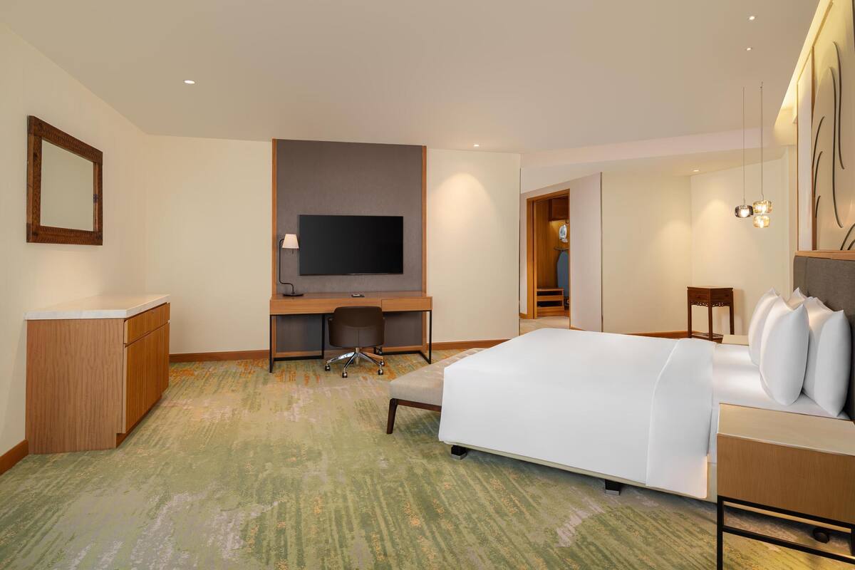 Ein Hotelzimmer mit Bett, Schreibtisch, Fernseher und begehbarem Kleiderschrank.