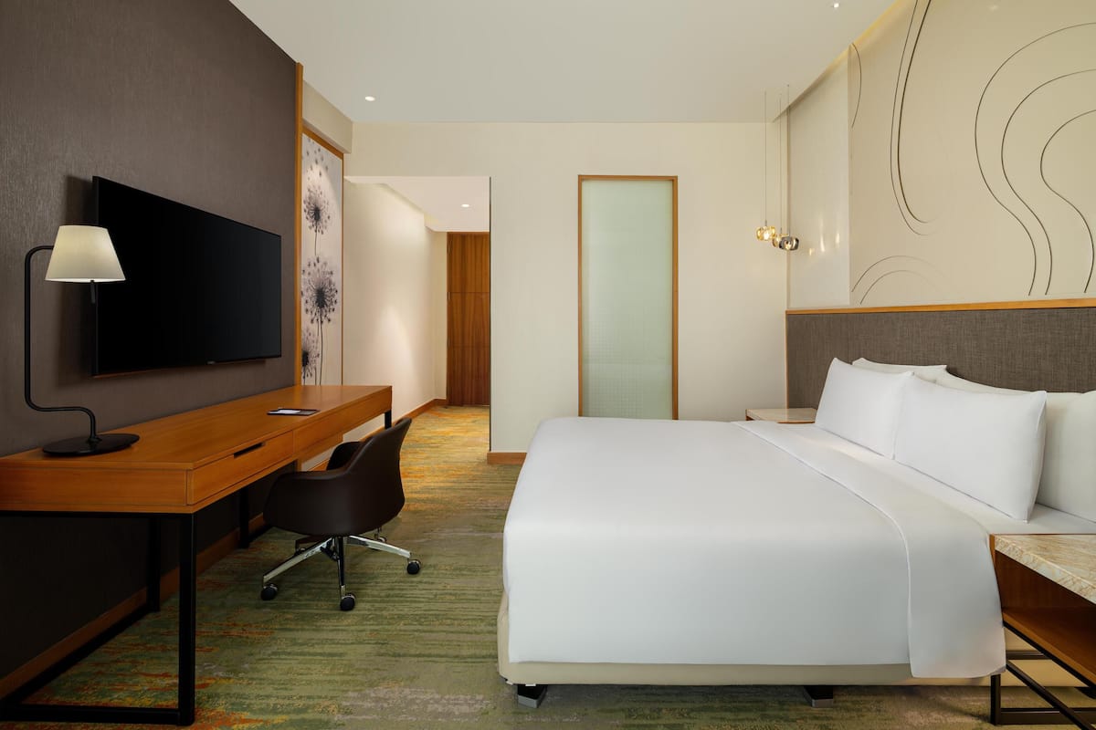Ein Hotelzimmer mit einem großen Bett, einem Schreibtisch mit Stuhl, einem Flachbildfernseher und einem modernen Wanddesign.