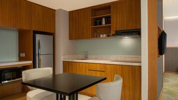 Cocina moderna con armarios de madera, encimera negra, refrigerador de acero inoxidable, horno integrado y televisor de pantalla plana montado en la pared.