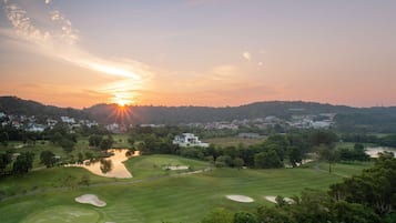 A golf course with sand bunkers and a pond, surrounded by trees and residential buildings in the background.
