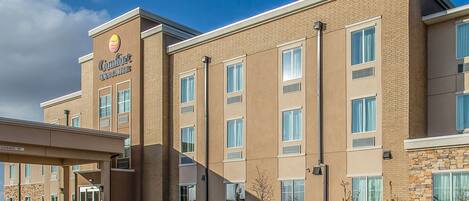 A Comfort Inn Suites building with a clear entrance, multiple windows, and a landscaped area with plants and rocks.
