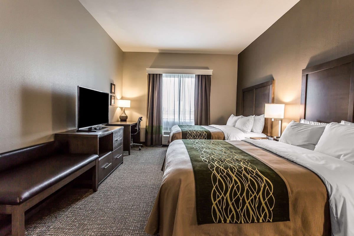 A hotel room with two beds, a TV, a desk, and a window with curtains.