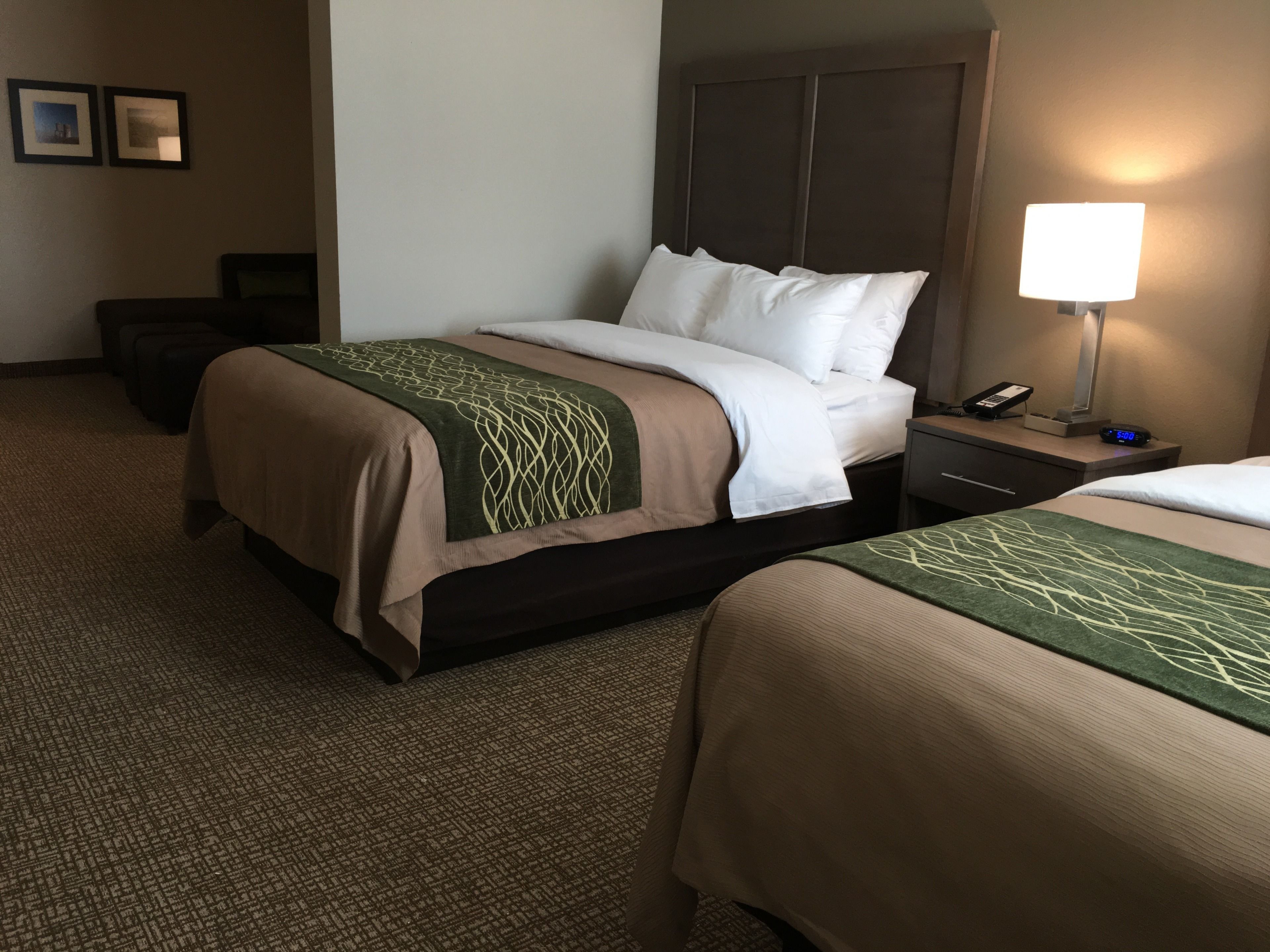 A hotel room with two beds, a nightstand with a lamp, a phone, and a small table.