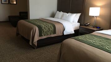 A hotel room with two beds, a nightstand with a lamp, a phone, and a small table.