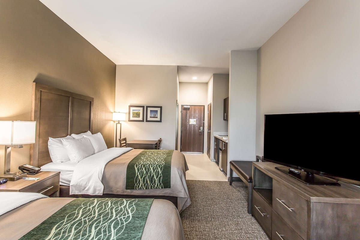 A hotel room with two beds, a television, a desk, and a bathroom visible in the background.