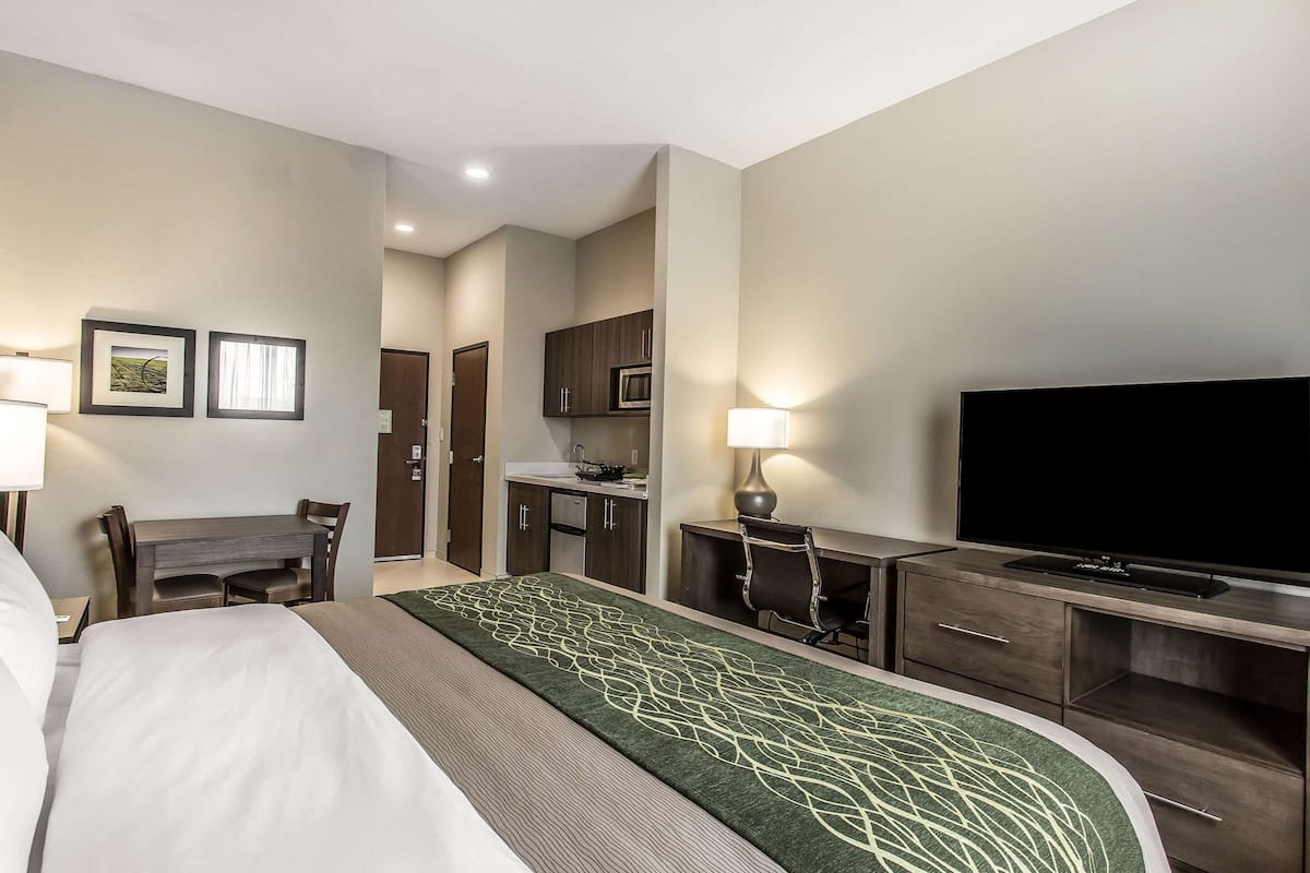 A hotel room with a bed, desk, chair, TV, and kitchenette.