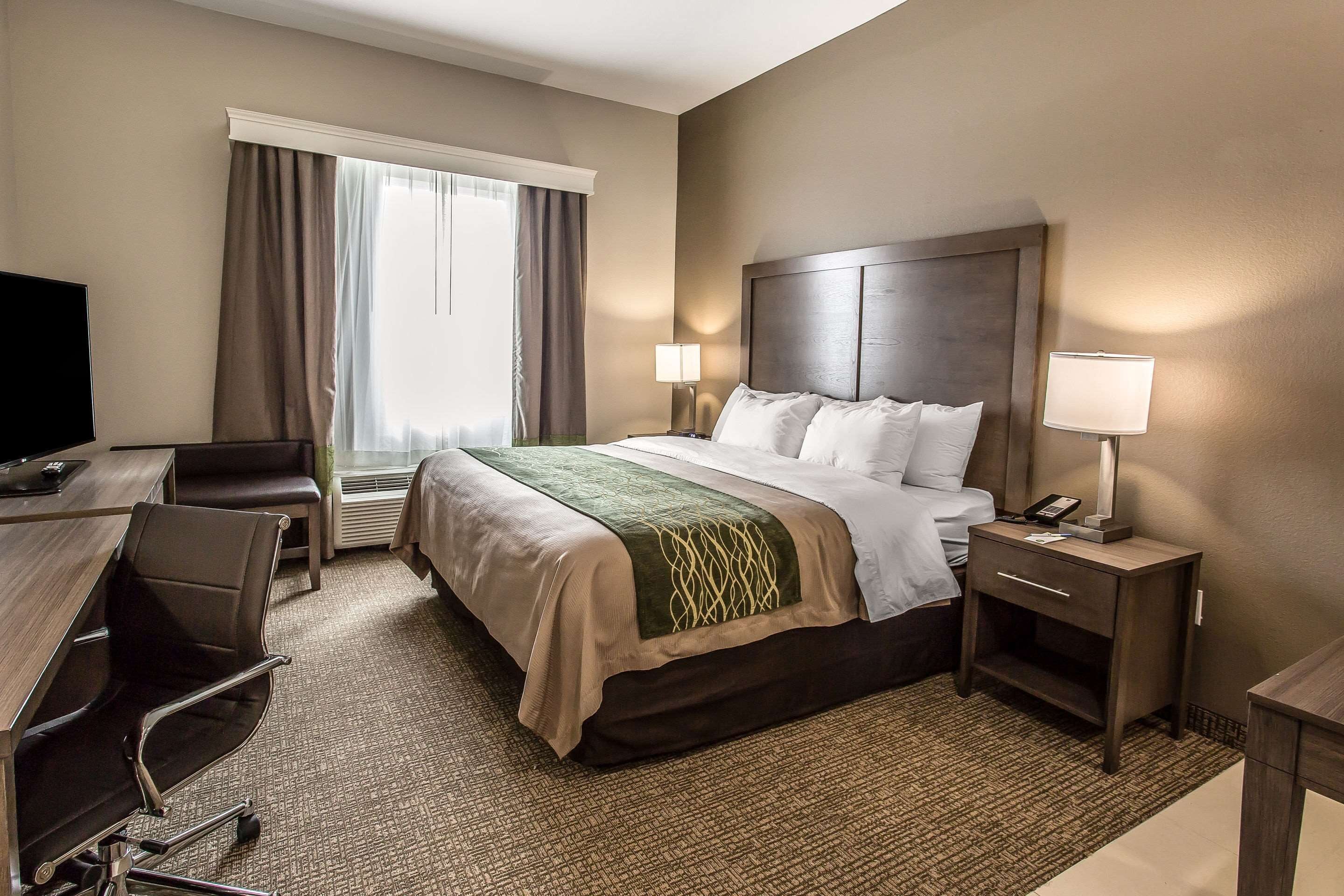 A hotel room with a bed, bedside tables, a desk, a chair, and a television.