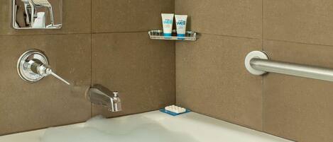 A bathroom with a bathtub, a handrail, a soap dish with two tubes, and a faucet.