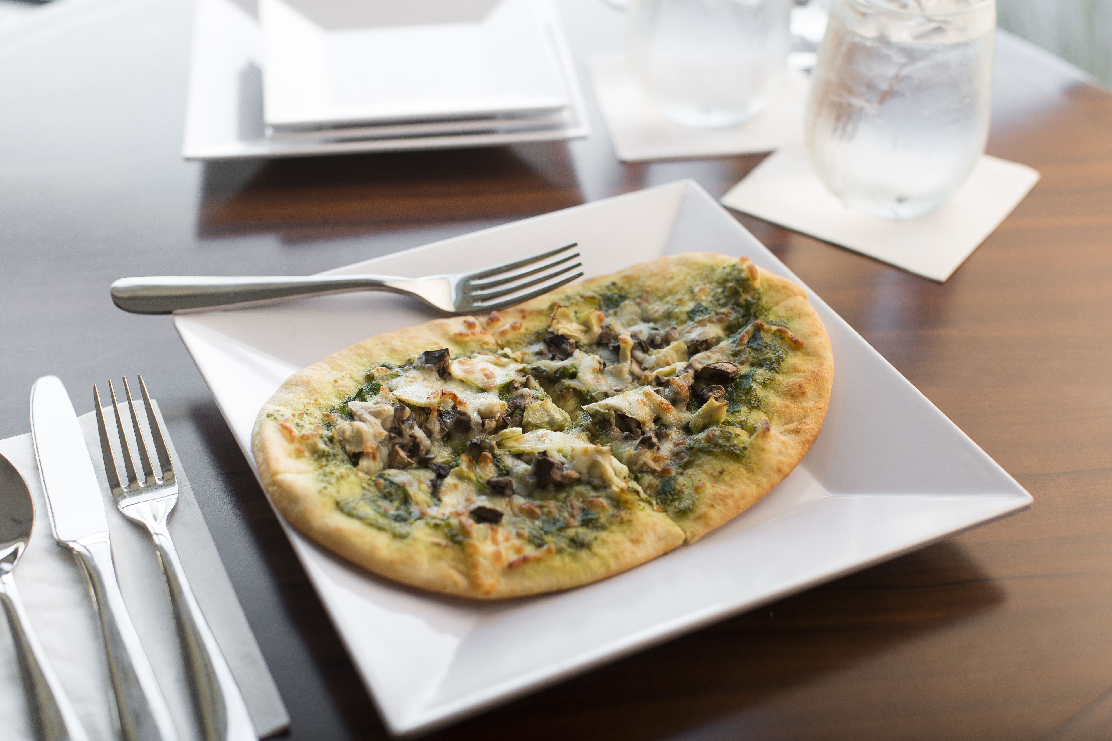 A pizza on a white plate with a fork beside it.