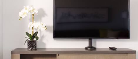 Un televisor de pantalla plana montado en una pared sobre un mueble de madera con una orquídea en maceta sobre su superficie.