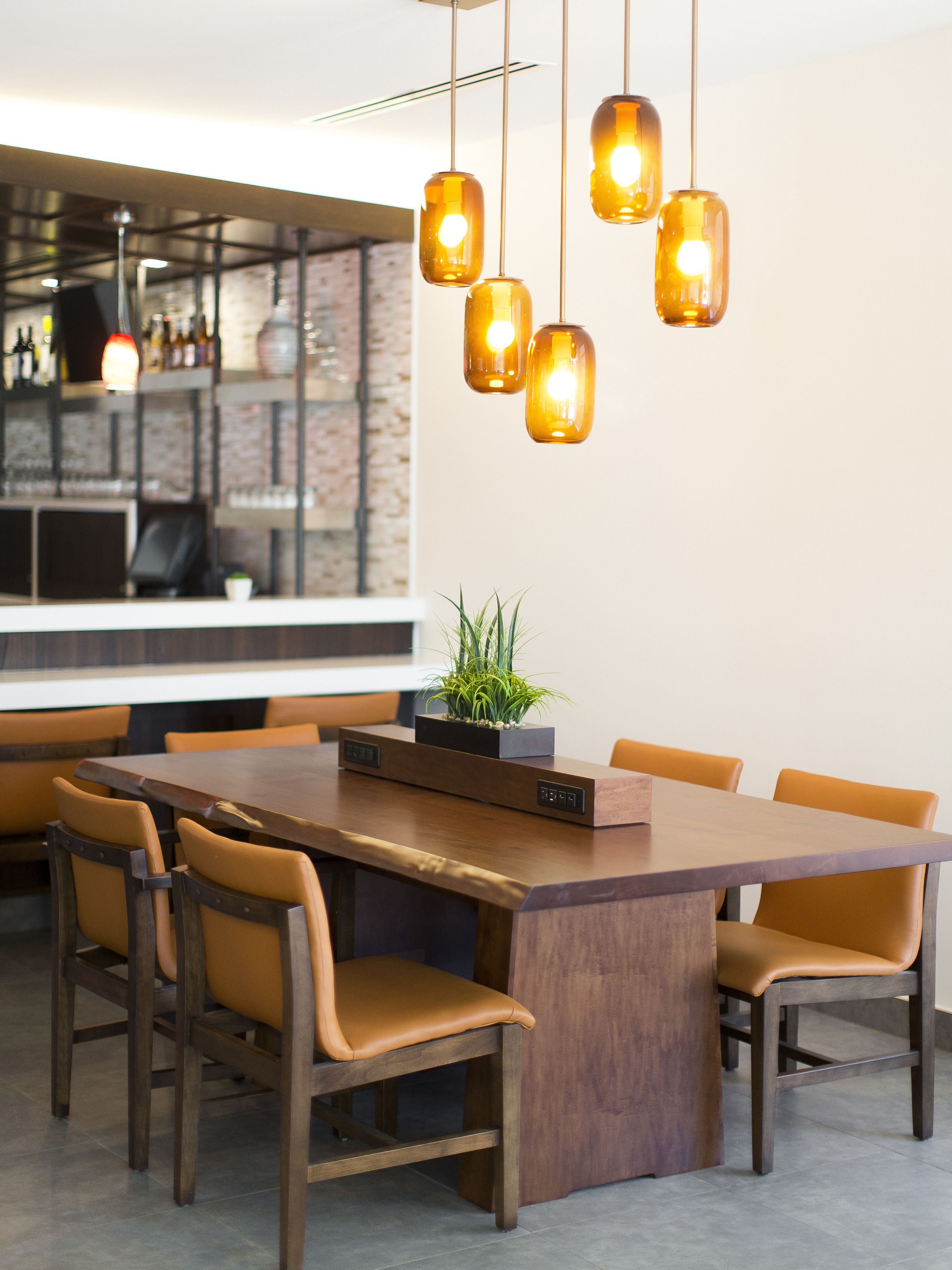 Un espace repas moderne avec une grande table en bois, six chaises et des luminaires suspendus.