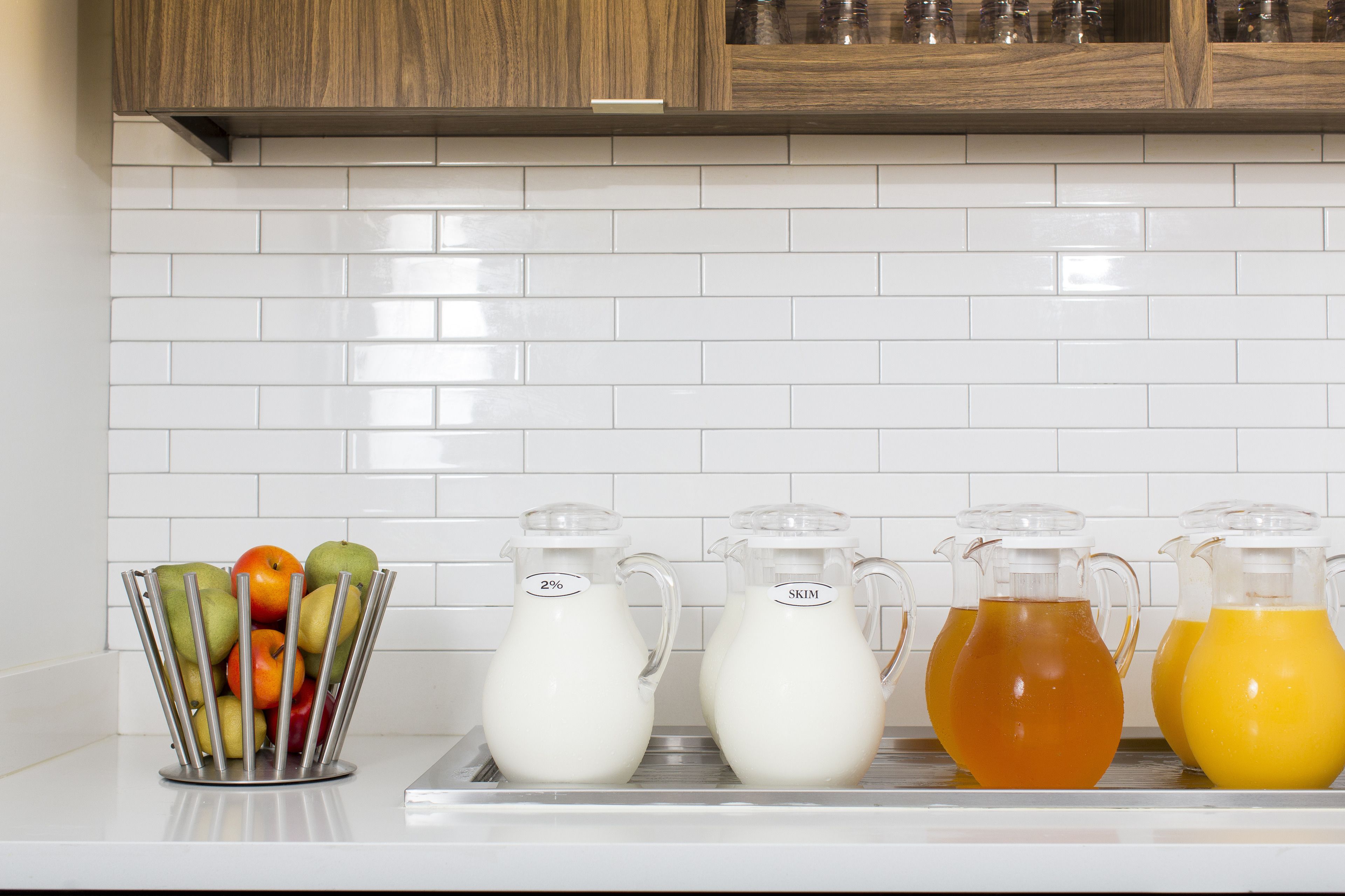A kitchen counter with a fruit basket and four pitchers of different liquids.