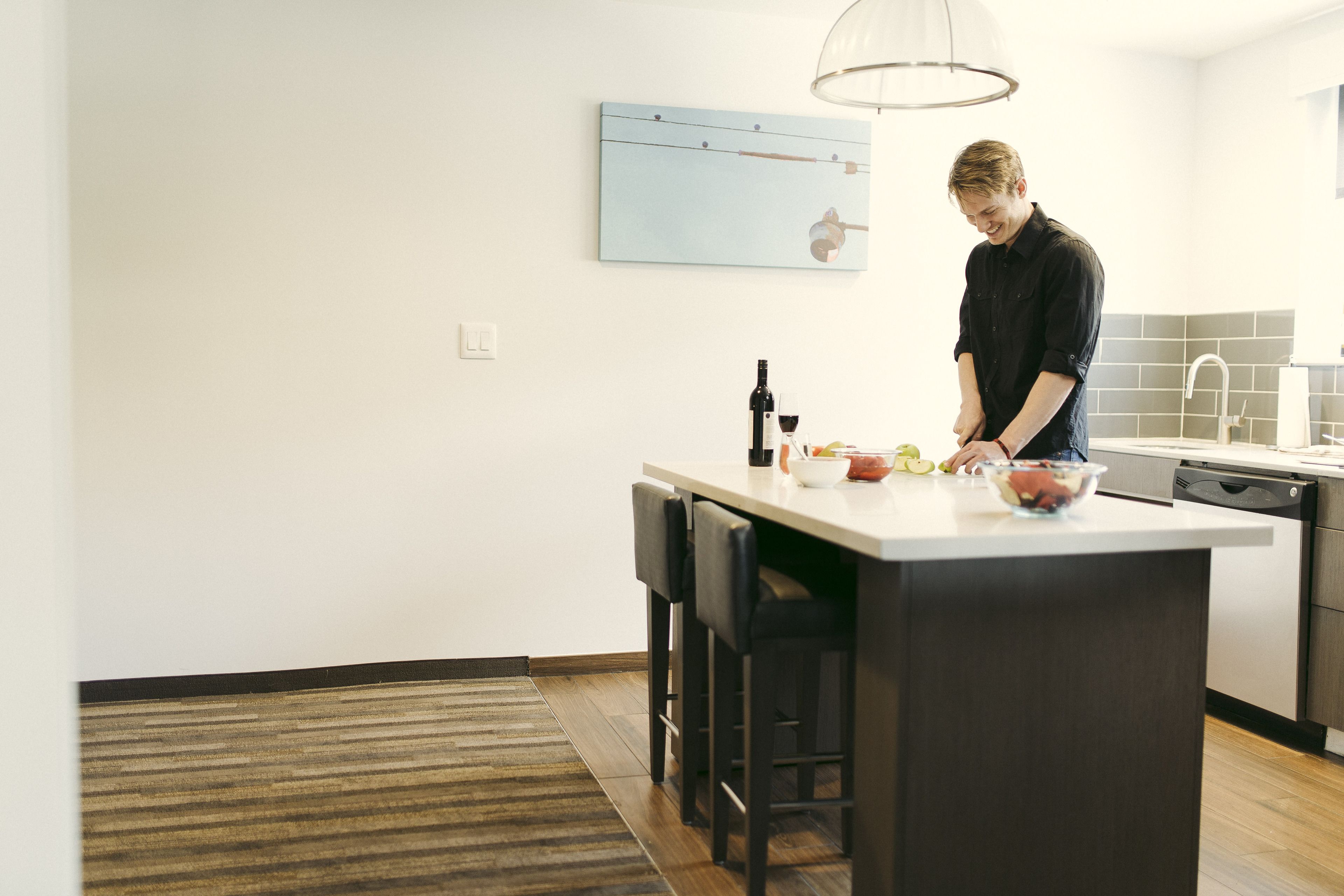 A modern kitchen with a large island, bar stools, a hanging light fixture, and a wall-mounted artwork.