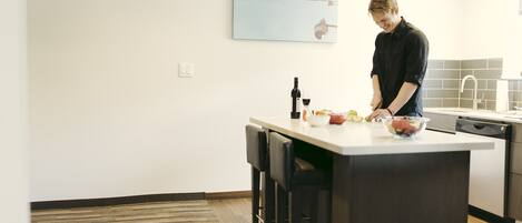 A modern kitchen with a large island, bar stools, a hanging light fixture, and a wall-mounted artwork.