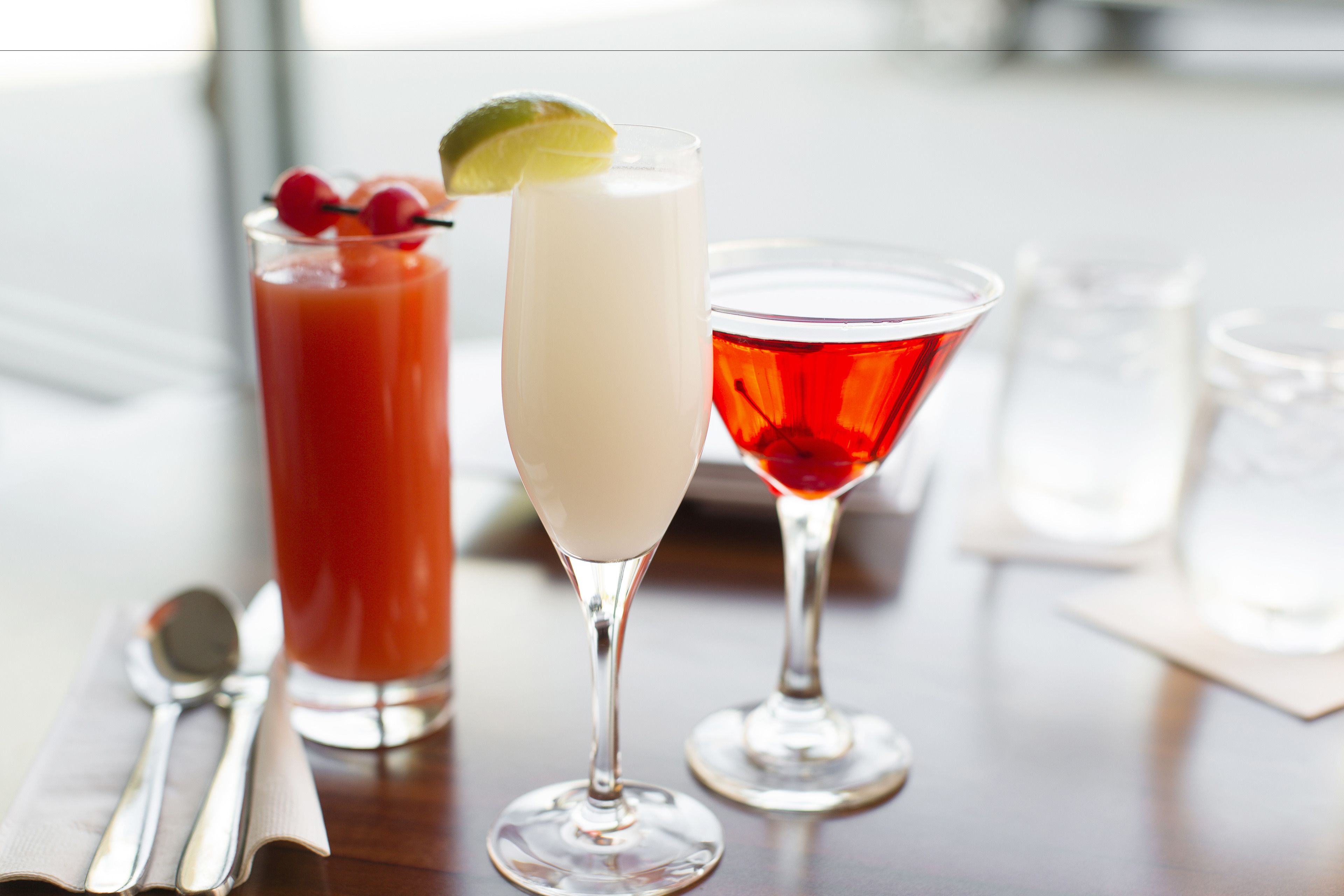 Three drinks on a table with a spoon and a napkin.