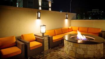 An outdoor seating area with a stone fire pit and orange cushions.