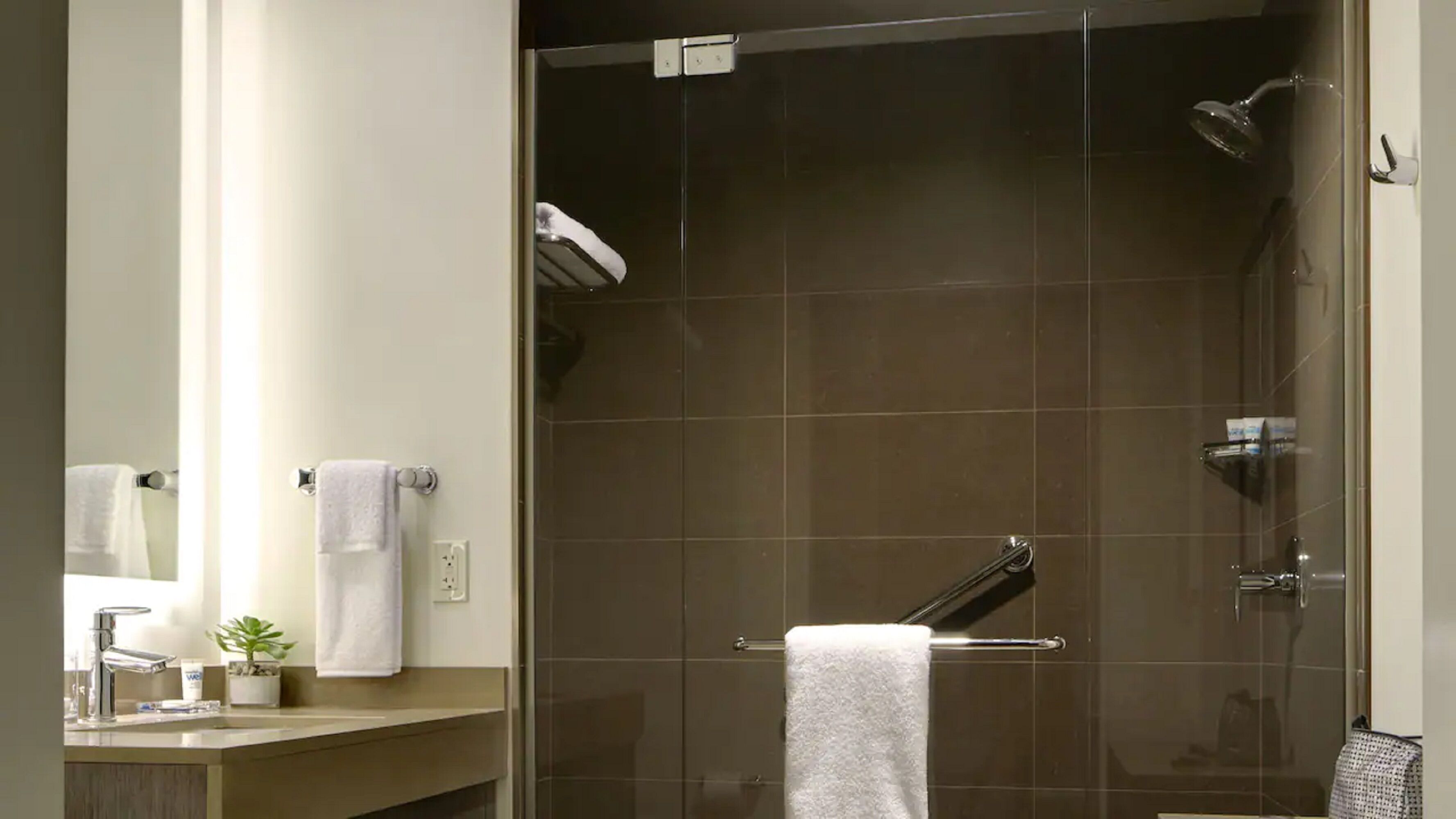 Ein modernes Badezimmer mit Duschkabine aus Glas, Waschbecken und Spiegel sowie einem Handtuchhalter.