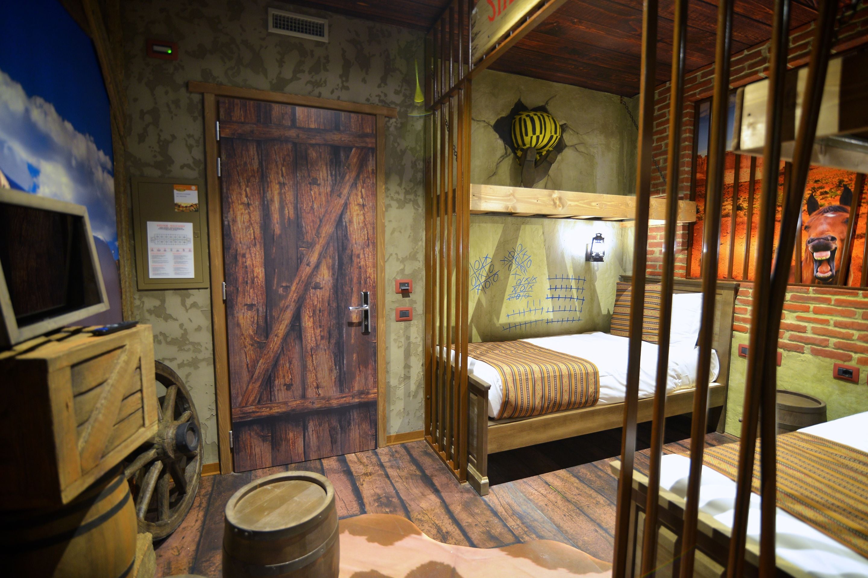 Ein rustikaler Raum mit einem Holzstockbett, einem Holztisch mit Fass und einem Wandgemälde eines Pferdes.