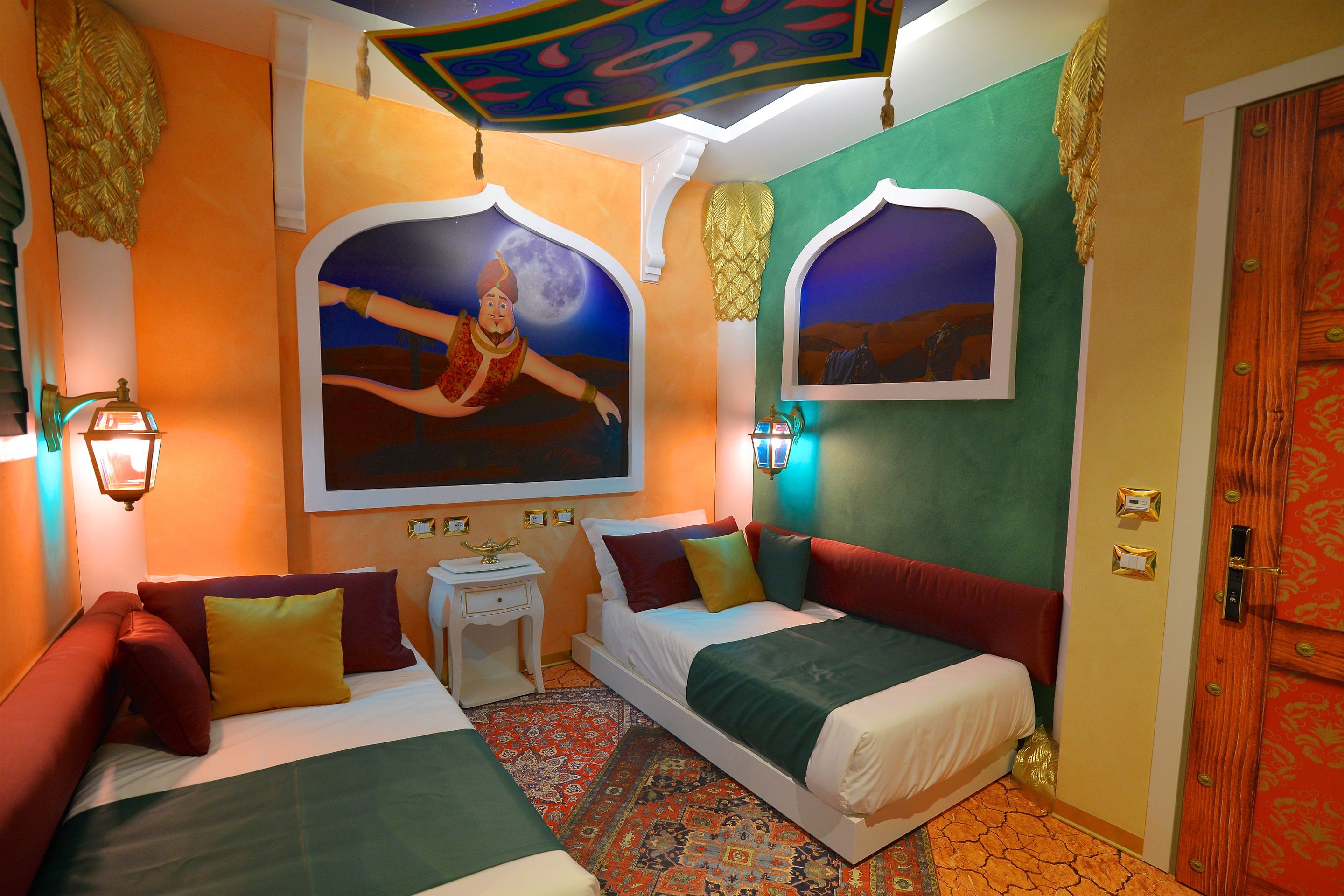 A room with two beds, a nightstand, a wall-mounted lamp, and a patterned rug.
